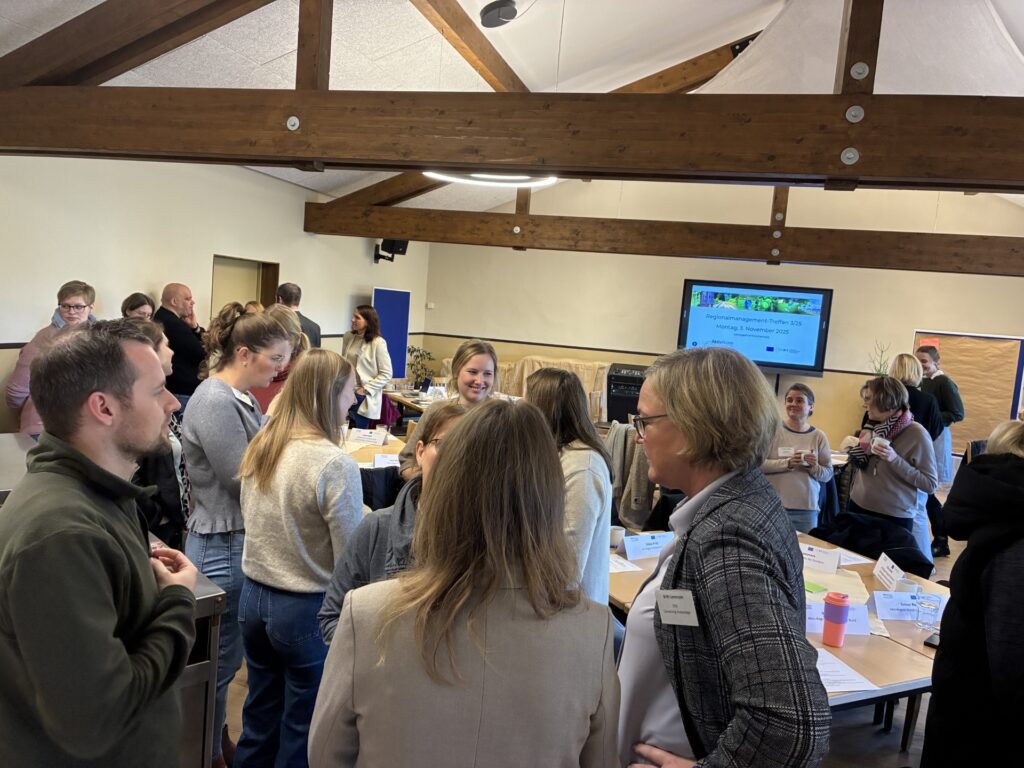 Viele Menschen stehen und sitzen in einem Raum und unterhalten sich